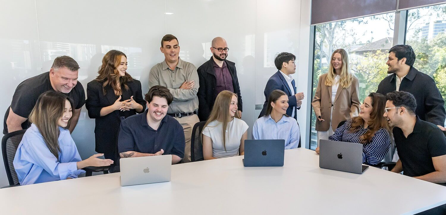 The team laughing together around a meeting-room table with laptops