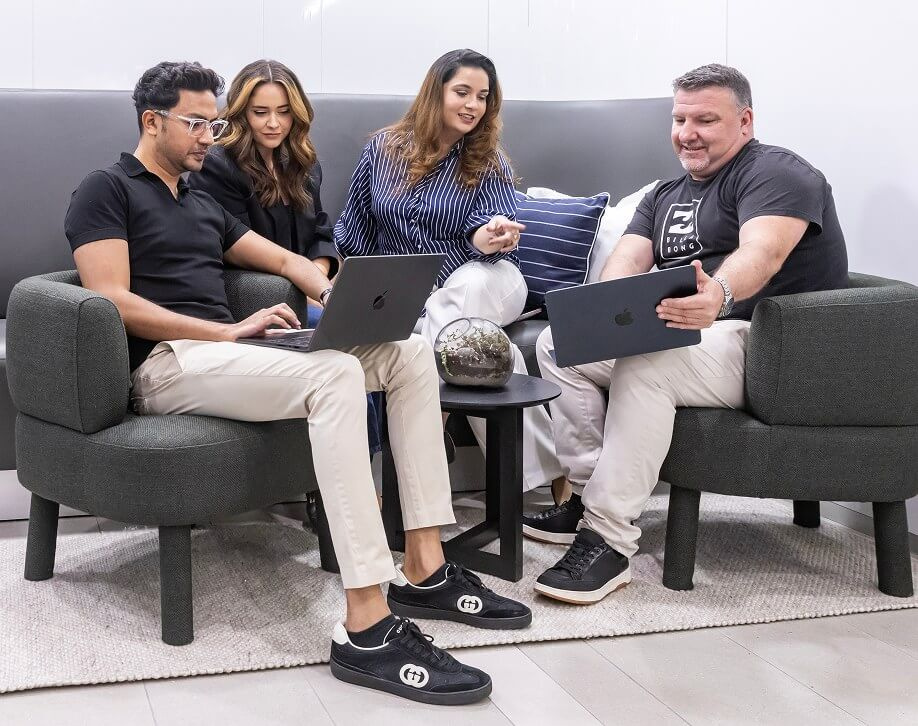 Four team members on lounge chairs reviewing work on their laptops
