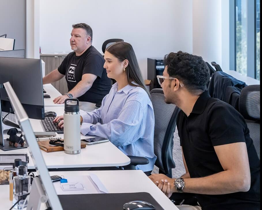 Three team members working side by side at a long desk