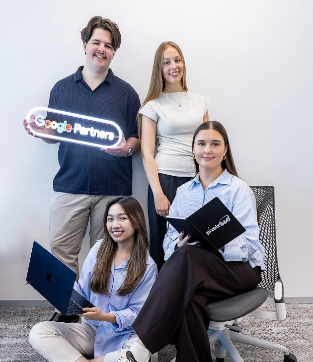 Four team members in the office, one holding a neon Google Partners sign